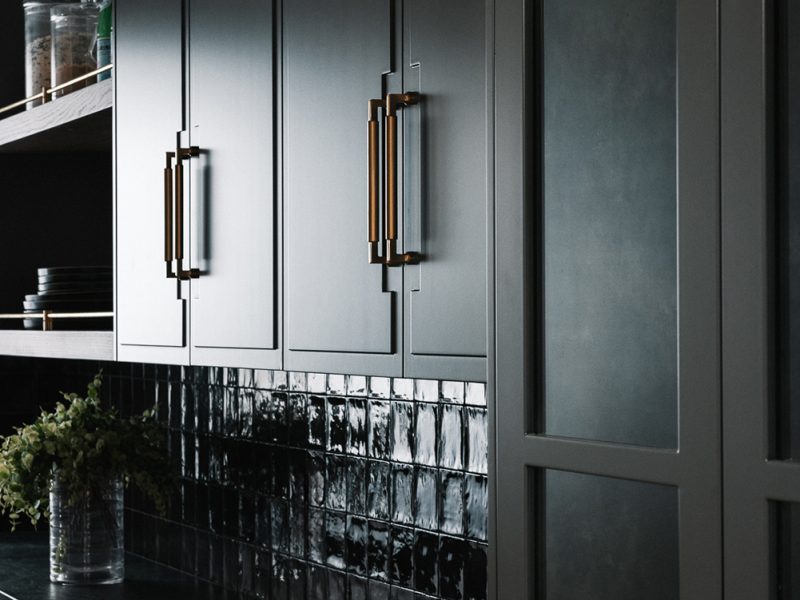 Dark pantry with custom doors, gold hardware, and black tile