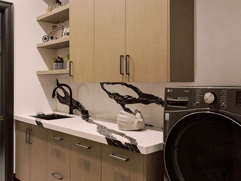 Light wood laundry room cabinets with black and white countertop