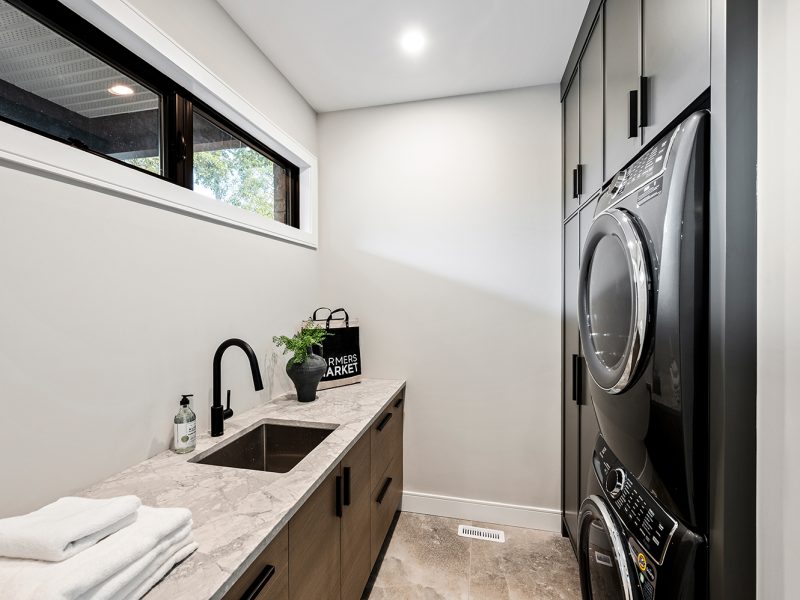 Dark oak and black laundry room cabinets around stackable machines
