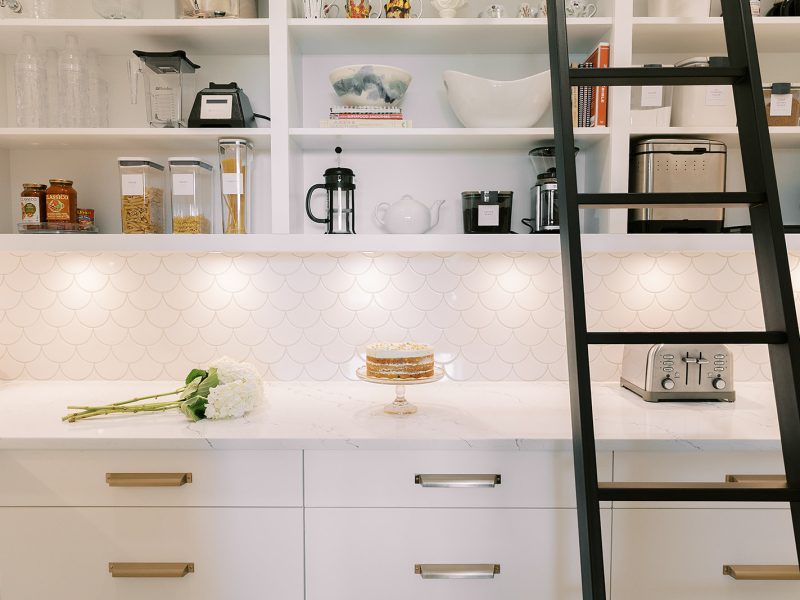 White pantry with open shelving, scalloped backsplash, and ladder